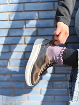 Zapatillas deportivas de cuero color peltre, con cordones negros y suela de goma blanca.