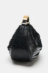 Bolso de mano negro de diseño fruncido con detalle de tiras y bolsillo interior con cremallera. Cuenta con un asa rígida metálica dorada y cierre principal mediante cremallera.