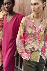 Blusa de manga larga con estampado floral en tonos rosados, verdes y beige. Presenta escote en pico con detalle de abalorios colgantes y cierre frontal con botones.