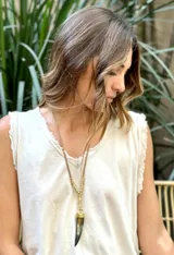 Collar largo con cordón de gamuza color beige, cuentas doradas y dije colgante en forma de cuerno o colmillo con remate metálico dorado.