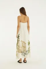 Vestido largo blanco de algodón con tirantes finos, escote recto y corte amplio en línea A. Presenta un estampado posicional tropical con palmeras, hojas de banano y arquitectura colonial.