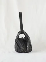 Bolso bandolera de cuero vacuno lavado color negro, con tachuelas plateadas y doradas en el cuerpo. Cuenta con cierre de cremallera, asa de hombro extraíble y bandolera regulable y desmontable.