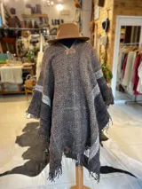 Poncho de lana virgen tejido en telar con diseño geométrico a rayas en tonos gris, marrón y celeste, con apliques de cuero en el escote y flecos en el ruedo.