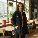 Sobre camisa tipo campera de jean color negro, con corte oversize, cuello italiano, mangas largas y cierre frontal con botones metálicos. Presenta bolsillos frontales con solapa y ruedo deshilachado.