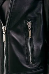 Chaqueta tipo biker de cuero negro con cierre frontal asimétrico, solapas con broches metálicos, bolsillos laterales con cierre y detalles de costuras acolchadas en la parte inferior.