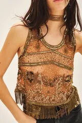 Top corto sin mangas con escote redondo, confeccionado en tul bordado con lentejuelas, piedras y canutillos. Presenta un diseño con flecos de mostacillas en el ruedo y una tira larga decorativa al cuello.