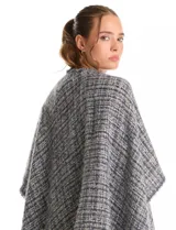 Ruana de tejido tipo tweed en tonos azul y gris con destellos de lurex. Presenta un diseño abierto con terminaciones desmechadas y flecos en todo el borde inferior.
