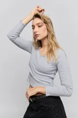 Remera de manga larga en tejido acanalado color gris, con escote en V y detalle de puntilla en el borde del cuello.