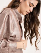 Camisa oversized con terminación metalizada color gris plomo. Tiene botones a tono en el delantero, largo por debajo de la cadera y tajos a los costados.