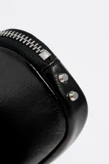 Monedero ovalado color blanco de la marca Bimba y Lola, confeccionado en piel. Cuenta con cierre de cremallera, tirador metálico, logo estampado y ribetes metálicos.