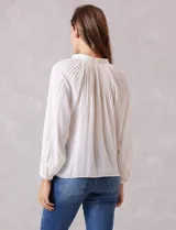 Blusa de gasa con plisado soleil, cuello a la base fruncido con escote en V regulable mediante lazos, y mangas largas abullonadas con puños sastreros.