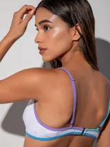 Top de bikini blanco con diseño de triángulos cruzados en el frente y vivos de colores celeste y lila. De breteles finos y con broche en la espalda.