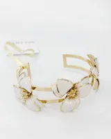 Pulsera rígida abierta de metal dorado, con diseño de flores esmaltadas en color blanco con vetas marmoladas y centro texturizado dorado.