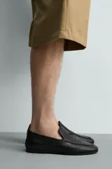 Mocasín de cuero negro con diseño liso, detalle de bordón en el empeine, horma redonda y suela ultrafina.