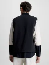 Chaleco negro acolchado con cuello alzado, cierre de cremallera, bolsillos con botón a presión y logo de Calvin Klein en el pecho.