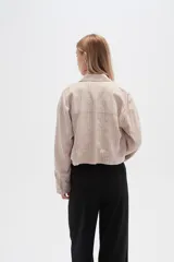 Chaqueta cropped de manga larga, color blanco con finas rayas verticales en tono claro. Presenta cuello camisa, cierre frontal con botones de madera y dos bolsillos delanteros con tapa a la altura del pecho.