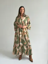 Vestido largo verde con estampado botánico en tonos tostados, escote en V con botones frontales, mangas largas abullonadas y diseño en niveles con volados.