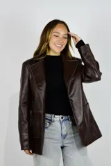 Blazer de cuero marrón con diseño recto y calce relajado. Cuenta con cierre frontal de un botón, solapas clásicas y bolsillos frontales parche.