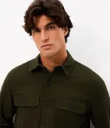 Camisa de manga larga confeccionada en sarga de algodón color verde militar. Presenta cuello inglés, cierre frontal con botones y dos bolsillos con solapa en el pecho.