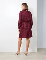 Vestido corto color borgoña con estampado geométrico, de gasa laminada con cuello alto entrelazado, manga larga raglán, cintura elastizada y espalda con abertura ojal y botones.