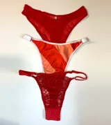 Pack de tres bombachas de distintos estilos: una de microtul roja con volados, una colaless con estampado a rayas rojas y naranjas y una tanga de encaje roja.