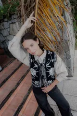 Chaleco tejido de punto con diseño floral en contraste, cierre frontal con lazos y terminaciones con guardas geométricas.