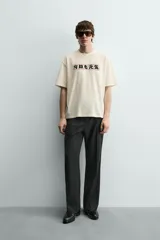 Camiseta relaxed fit color crema, con cuello redondo y manga corta. Presenta un estampado frontal con caracteres japoneses en negro y contorno rojo.
