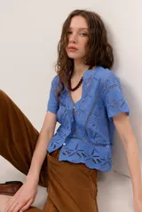 Camisa azul de manga corta confeccionada en tejido broderie con diseño calado y floral. Cuenta con escote en V y cierre frontal de botones.
