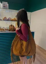 Cartera de hombro grande de gamuza color camel con flecos en el borde inferior.