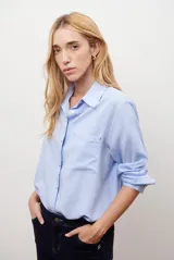 Camisa blanca de manga larga con cuello clásico, cierre de botones frontal y bolsillo de parche en el pecho.