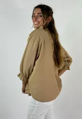 Blusa color beige con cuello mao, mangas 3/4 con puños elásticos y detalle de diseño geométrico texturizado en el frente.