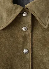Chaqueta corta de piel de serraje color marrón, con diseño recto, cuello camisero, manga larga y cierre frontal de botones metálicos. Cuenta con dos bolsillos de parche con solapa en la parte delantera y forro interior.
