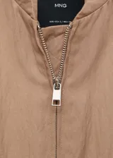 Chaqueta estilo bomber color beige, con cuello de tira, cierre frontal de cremallera, bajo y puños elásticos fruncidos y dos bolsillos laterales.