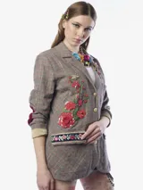 Blazer de corte sastre con estampado de cuadros en tonos grises y líneas rojizas. Presenta detalles bordados de flores con lentejuelas en el frente, parches en los codos, solapa clásica y cierre frontal con botones metálicos. Incluye bolsillos con solapas decoradas con bordados florales y un broche floral con cristales en la solapa.