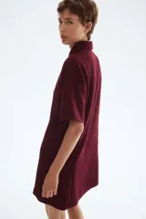 Vestido corto de tejido bouclé color bordó, con corte evasé, cuello camisero y tapeta de botones dorados. Posee mangas cortas y costuras princesa tanto adelante como atrás.