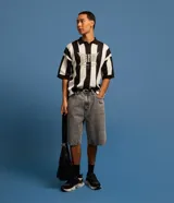 Bermuda de jean estilo baggy, color negro gastado, con bolsillos, cierre de botón y cremallera, y pespuntes contrastantes.