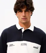 Buzo masculino confeccionado en algodón con felpa y diseño de bloques rayados en color azul marino y blanco. Presenta cuello polo, cierre frontal parcial con botones, manga larga y estampa frontal con íconos y texto.
