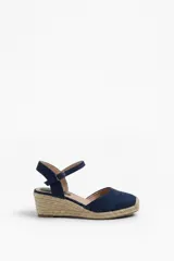 Sandalia de plataforma con cuña de yute y suela texturizada, color beige. Cuenta con puntera cerrada, diseño destalonado y tira ajustable al tobillo con hebilla metálica.