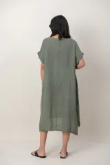 Vestido midi de lino color beige, de corte holgado y silueta acampanada. Cuenta con cuello redondo, mangas cortas amplias, bolsillos laterales y detalles de recortes horizontales en la falda con terminación asimétrica más larga en la parte trasera.