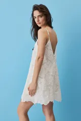 Vestido corto blanco de corte en A, confeccionado en tela con diseño de broderie floral y bordes scalloped. Cuenta con escote cuadrado y tirantes finos.