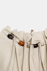 Top de cuello halter color beige, con detalle de volantes y abalorios de diferentes colores en el cuello. El bajo está acabado en elástico y tiene cierre en la espalda con abertura y lazada.