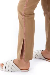 Pantalón de jean color café con corte recto, tiro alto, bolsillos delanteros y traseros, y tajos laterales en el ruedo. Presenta una franja vertical bordada en color rosa a lo largo de la costura lateral.
