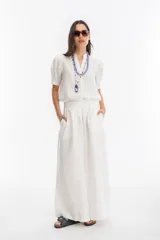 Pantalón blanco de lino, corte palazzo, tiro medio-alto, con tablas delanteras, elástico en la parte trasera y bolsillos laterales.