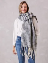 Bufandón de tejido soft con diseño de rayas horizontales en tonos gris y blanco, con terminación de flecos largos en los extremos.