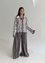 Camisa blanca de manga larga con delicados bordados florales verticales y detalles de encaje. Presenta cuello clásico, cierre frontal con botones y terminaciones festoneadas en los puños y el ruedo.