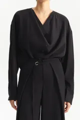 Camisa negra de manga larga con escote en V pronunciado y cruce frontal con botones. Presenta una silueta amplia y relajada.