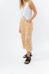 Pantalón de corte culotte y tiro medio, confeccionado en viscosa con estampado de hojas blancas sobre fondo color miel. Presenta una silueta amplia y fluida, con cintura elástica en la parte posterior y bolsillos laterales.