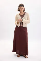 Cardigan de punto fantasía color crudo, con mangas largas y cierre delantero con tiras para atar. Presenta detalles de terminación en color negro en el ruedo y los puños.