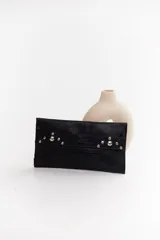 Sobre de cuero negro con solapa, cierre magnético y muñequera con tachas plateadas.