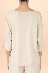 Suéter de punto color crema con cuello en V, mangas tres cuartos y detalle de costura vertical central. Presenta un diseño holgado con terminaciones acanaladas en puños y ruedo.